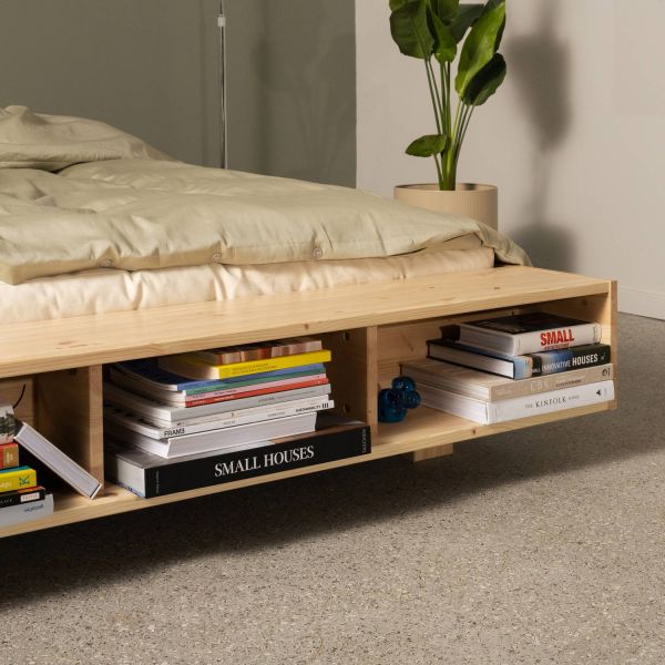 Close-up van het Karup futonbed Merge (FSC-gecertificeerd dennenhout) met ingebouwde boekenplank vol designboeken aan het ‘zwevende’ voeteneind.