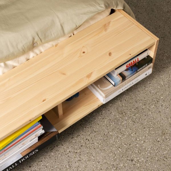Close-up van ingebouwde boekenplank in het ‘zwevende’ voeteneind van Karup Merge futonbed (FSC-dennenhout) vol designboeken.