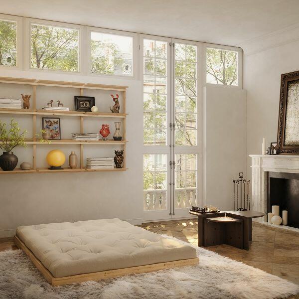 Karup Design slaapbank Flip uitgeklapt tot laag futonbed (140 × 200 cm); dikke off-white futonmatras op FSC-gecertificeerd dennenhouten boxframe in lichte woonkamer met wandplanken en open haard.